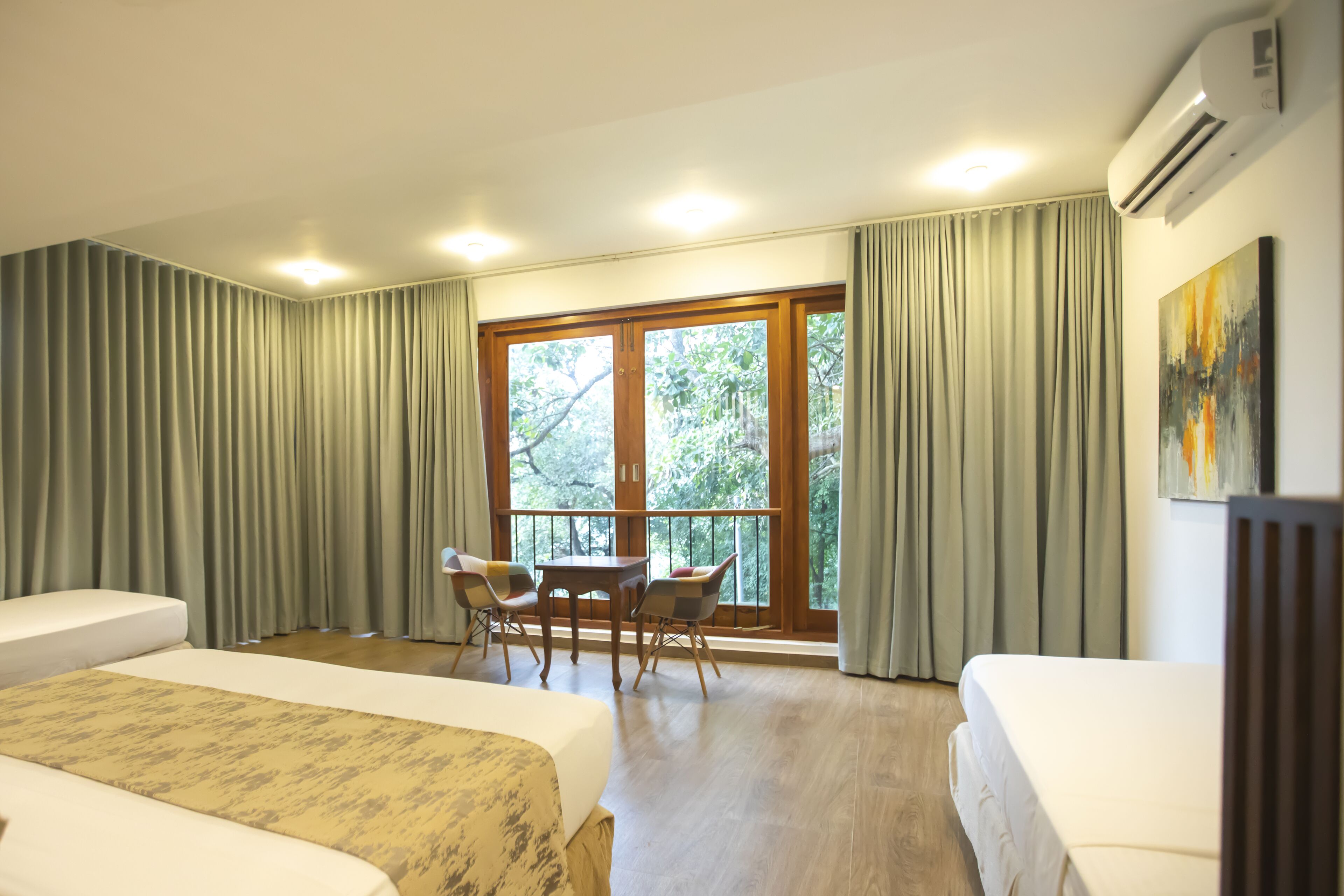 Habitación de hotel con dos camas, una mesa de comedor, sillas, un ventanal con cortinas y un equipo de aire acondicionado.