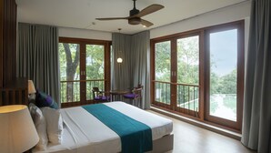 A hotel room with a large bed, a ceiling fan, a balcony with a table and chairs, and large windows offering a view of the outdoors. - Birds Park Polgahawela (Alawwa)