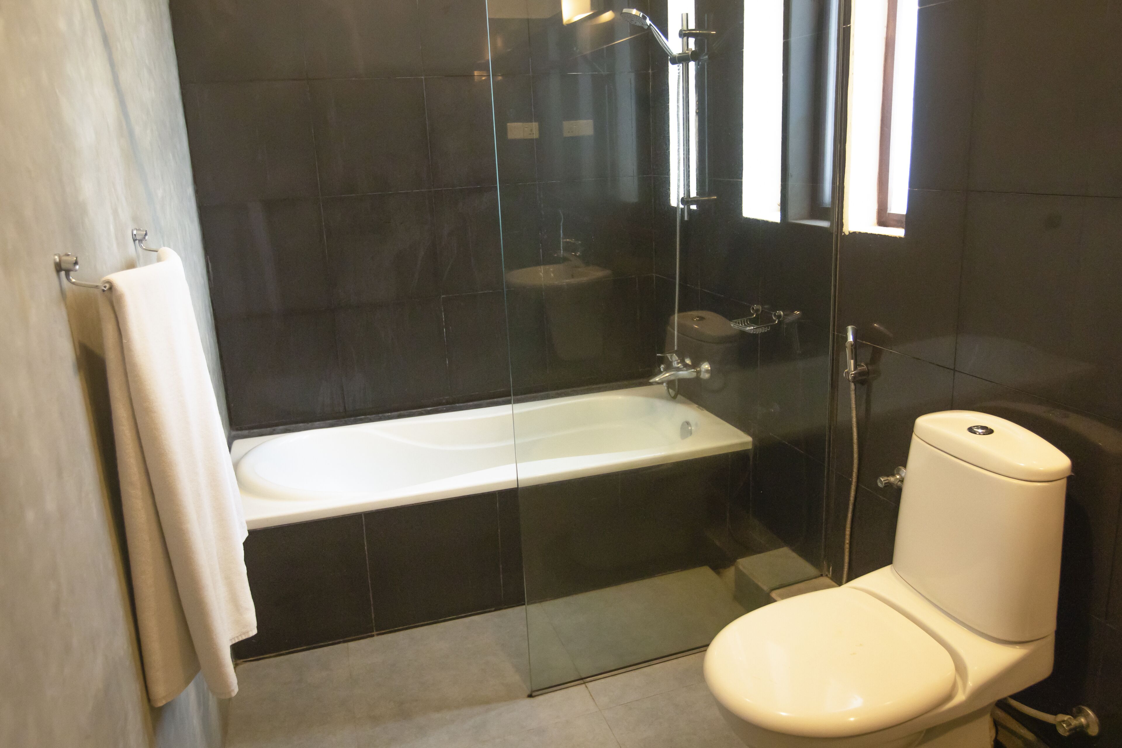 A modern bathroom with a glass-enclosed shower, a white bathtub, and a toilet.