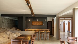 A modern dining area with a long wooden table and chairs, a stone wall, and a wooden bar counter. - Birds Park Polgahawela (Alawwa)
