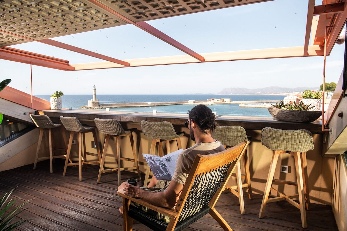 A person sitting at a wooden table with a view of the sea and a lighthouse.