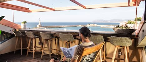A person sitting at a wooden table with a view of the sea and a lighthouse.