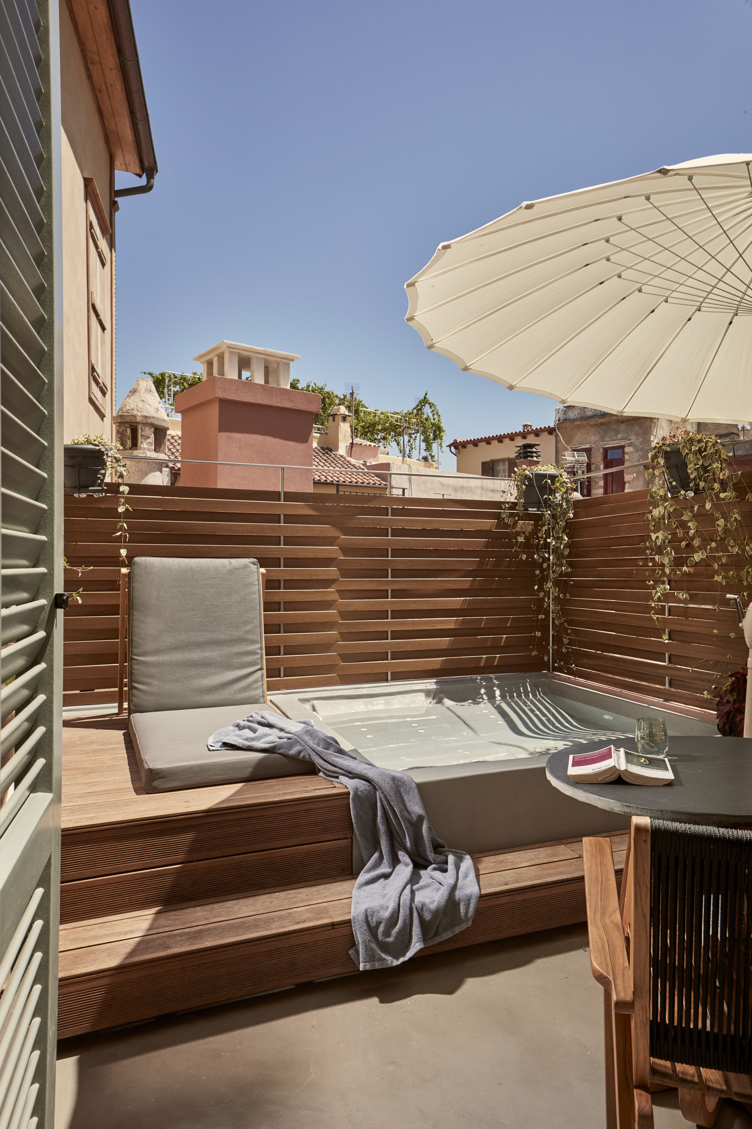 A rooftop patio with a wooden deck, a cushioned seating area, a table with a book, and an umbrella.