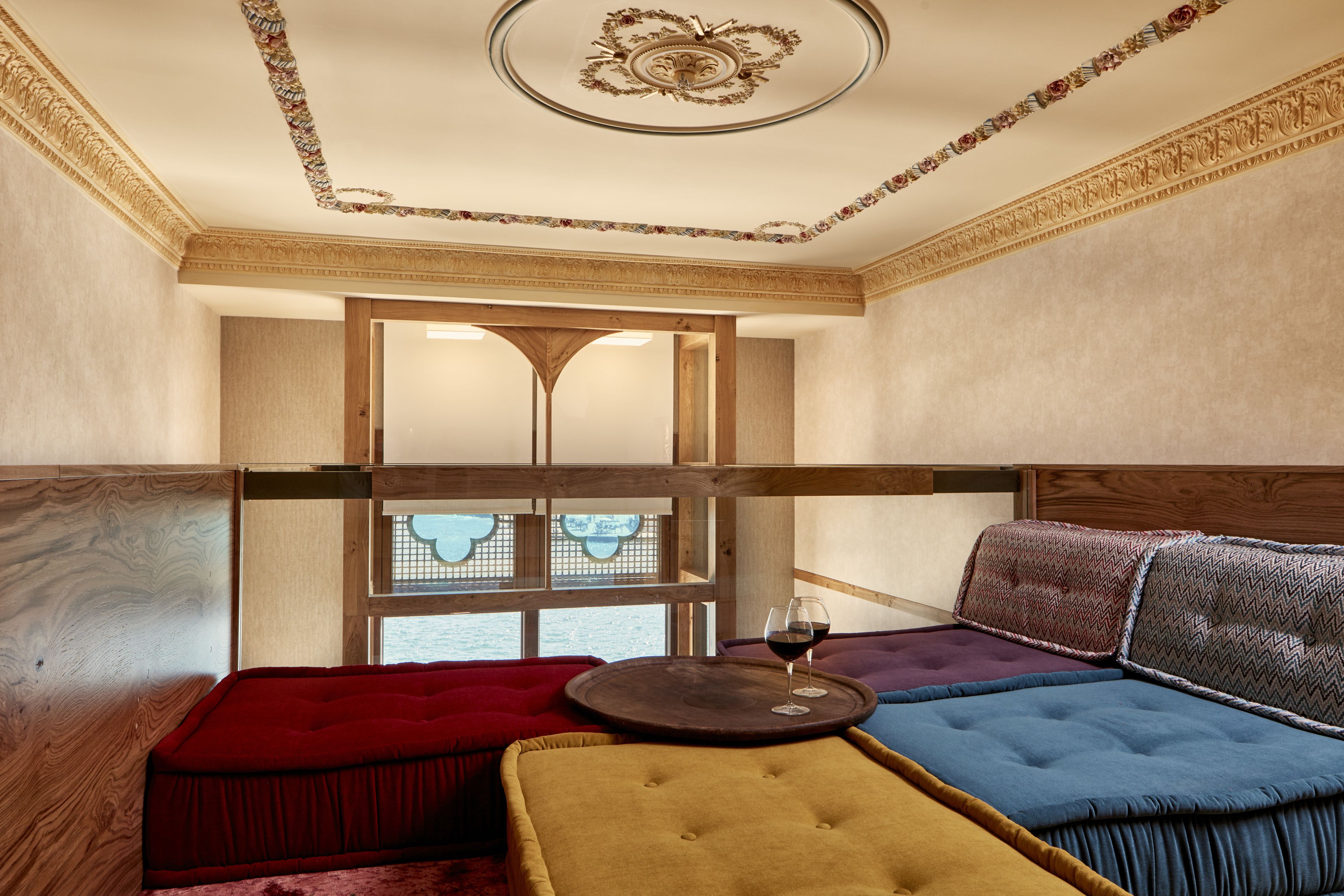 A room with a wooden ceiling, a large window, and a seating area with a round table and a glass of wine.