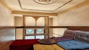Una habitación con techo de madera, un ventanal grande y una zona de estar con una mesa redonda y una copa de vino.