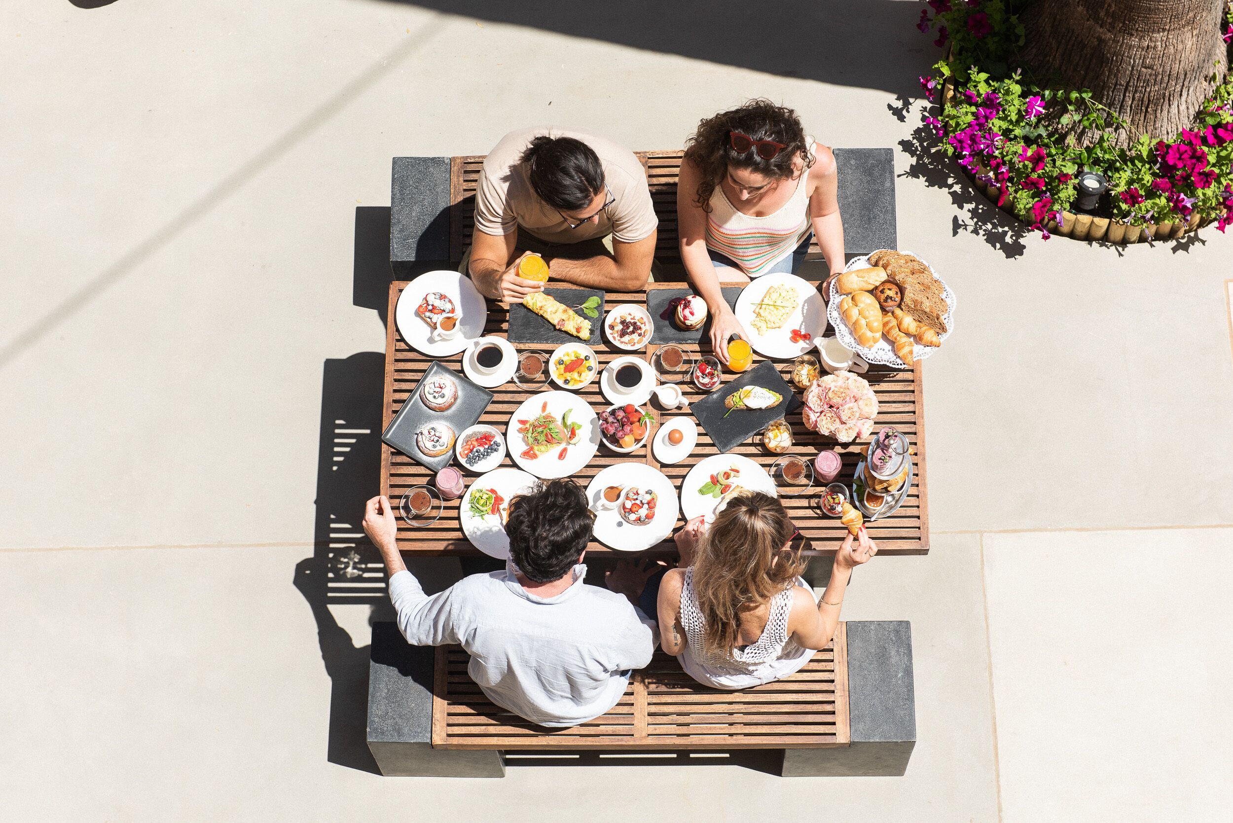 A top-down view of a dining table with various dishes and drinks, surrounded by people.
