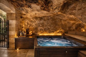 Een wellnessruimte met een jacuzzi, kaarsen en een stenen muur.