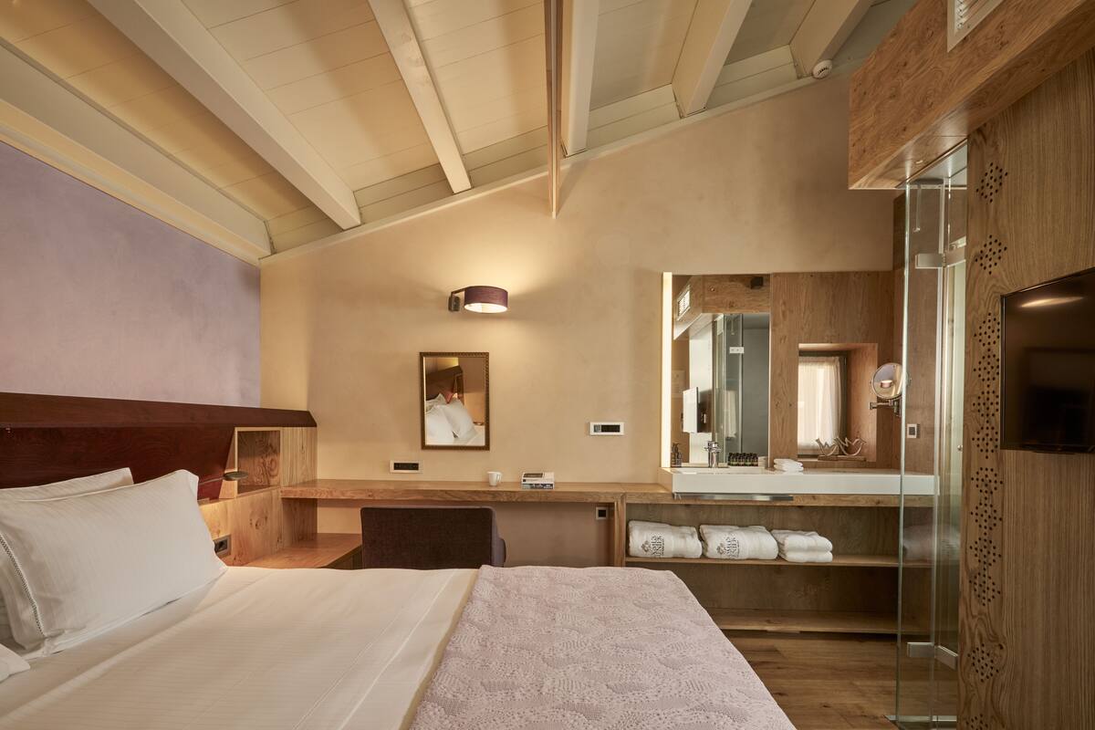 A hotel room with a bed, a desk, a mirror, and a glass shower enclosure.