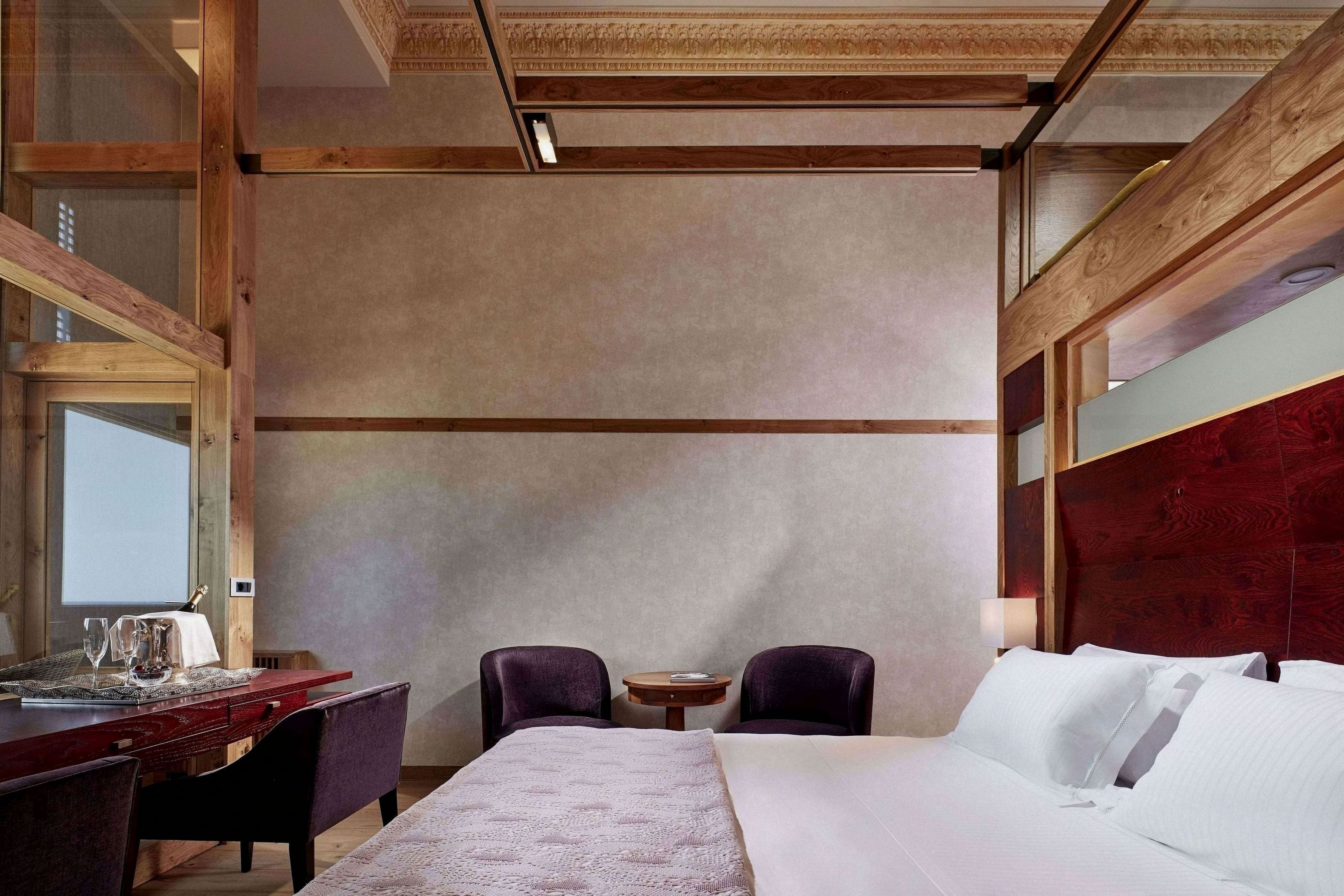 A hotel room with a large bed, a desk with a chair, two smaller chairs, a round table, and a mirror.