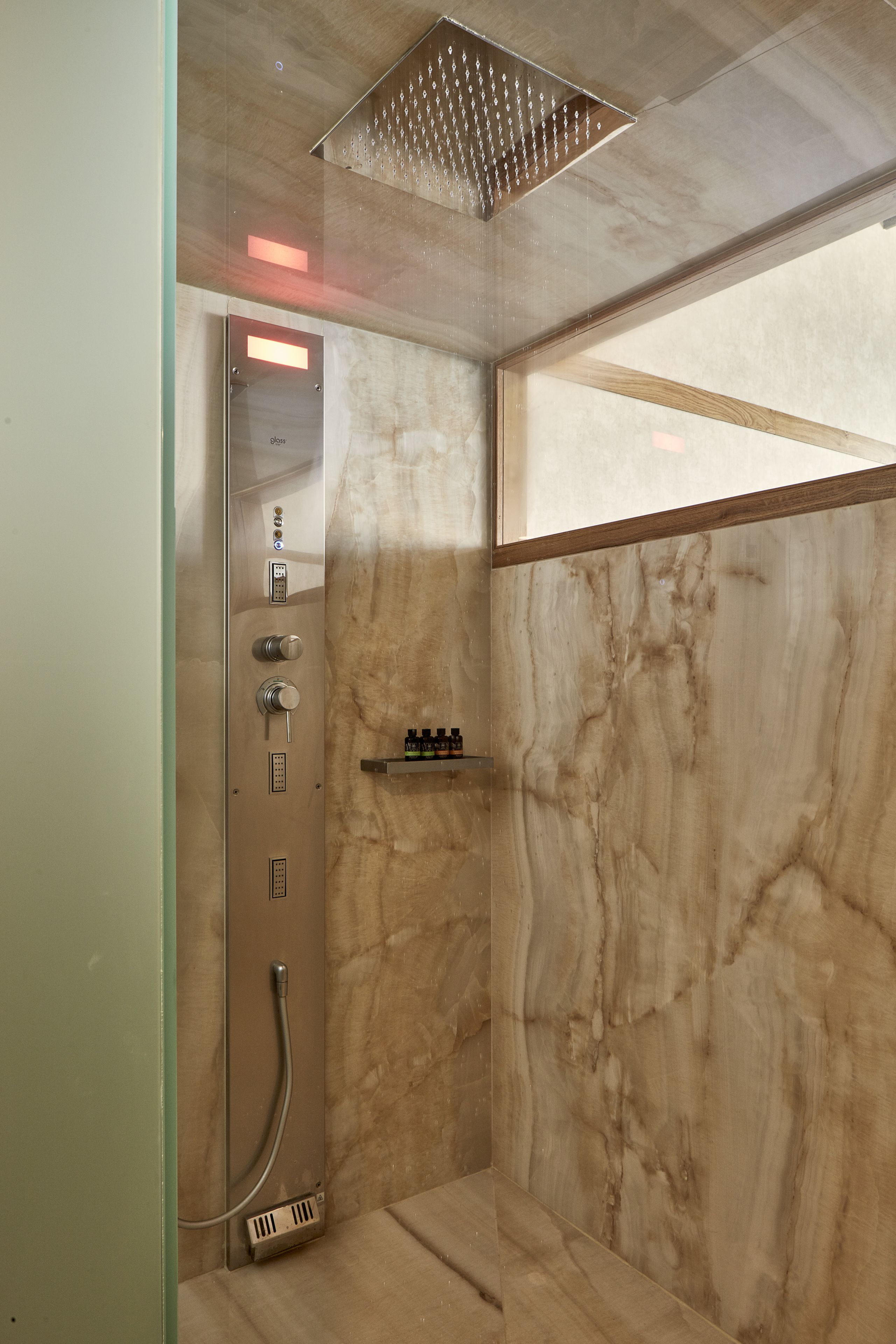 A modern shower with a control panel, marble walls, and a wooden accent.