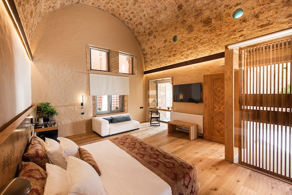 A bedroom with a large bed, a sofa, a TV, and a wooden floor. - Domus Renier Boutique Hotel, Member of Domus Elegance Collection (Chania)