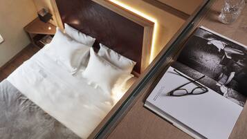 Una cama bien hecha con sábanas blancas, un cabecero de madera y una mesita de noche con una lámpara.