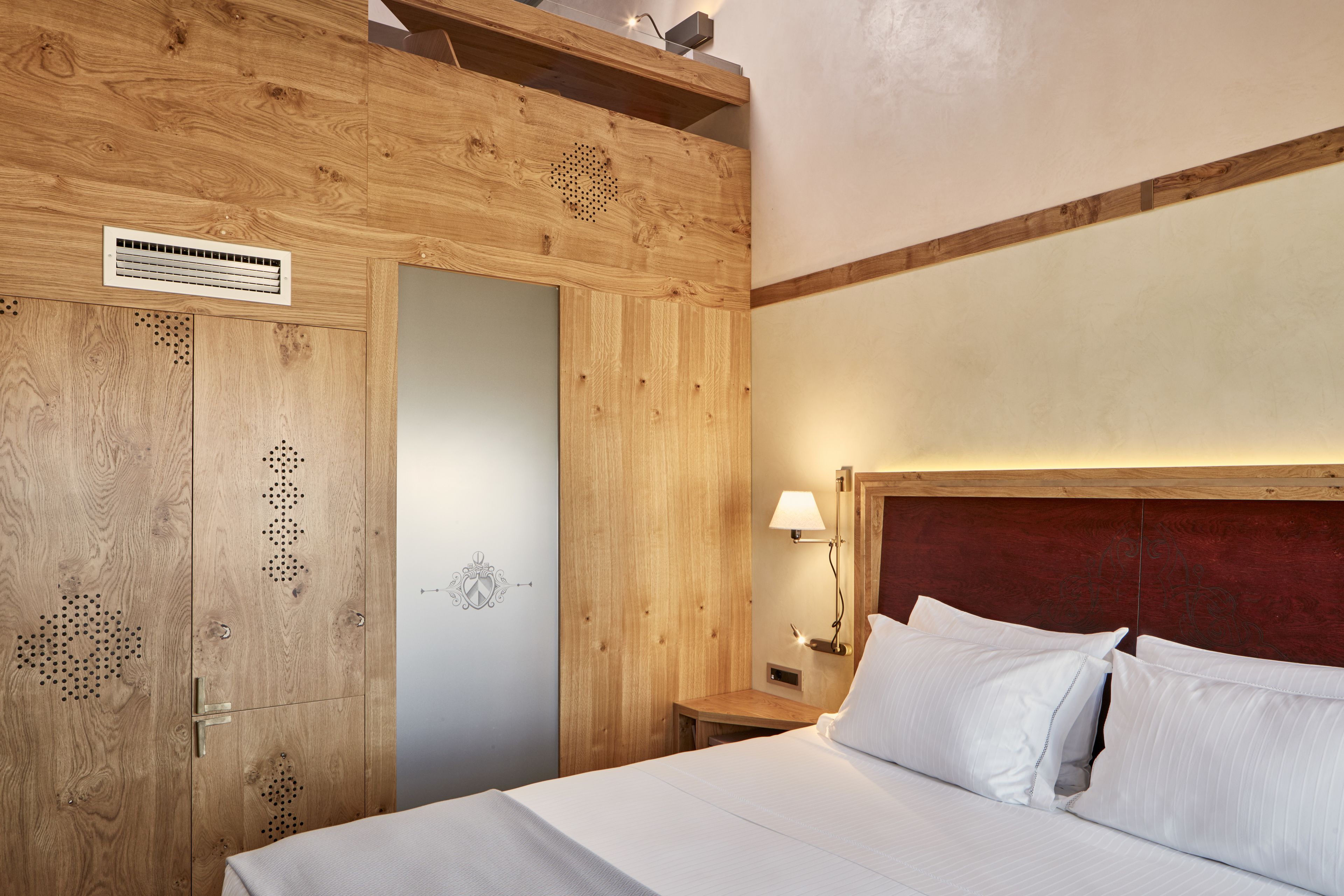 Una habitación con paneles de madera, una cama, una mesita de noche y una lámpara de pared.