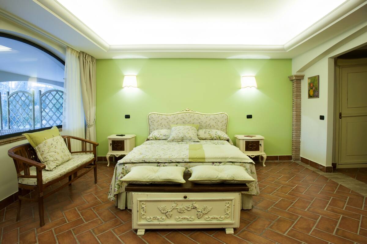 A bedroom with a bed, two bedside tables, a chair, a window with curtains, and a door.