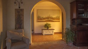 A living room with a striped armchair, a potted plant, a cabinet with glassware, and a painting on the wall. - La Vignola Country Hotel (Ceprano)