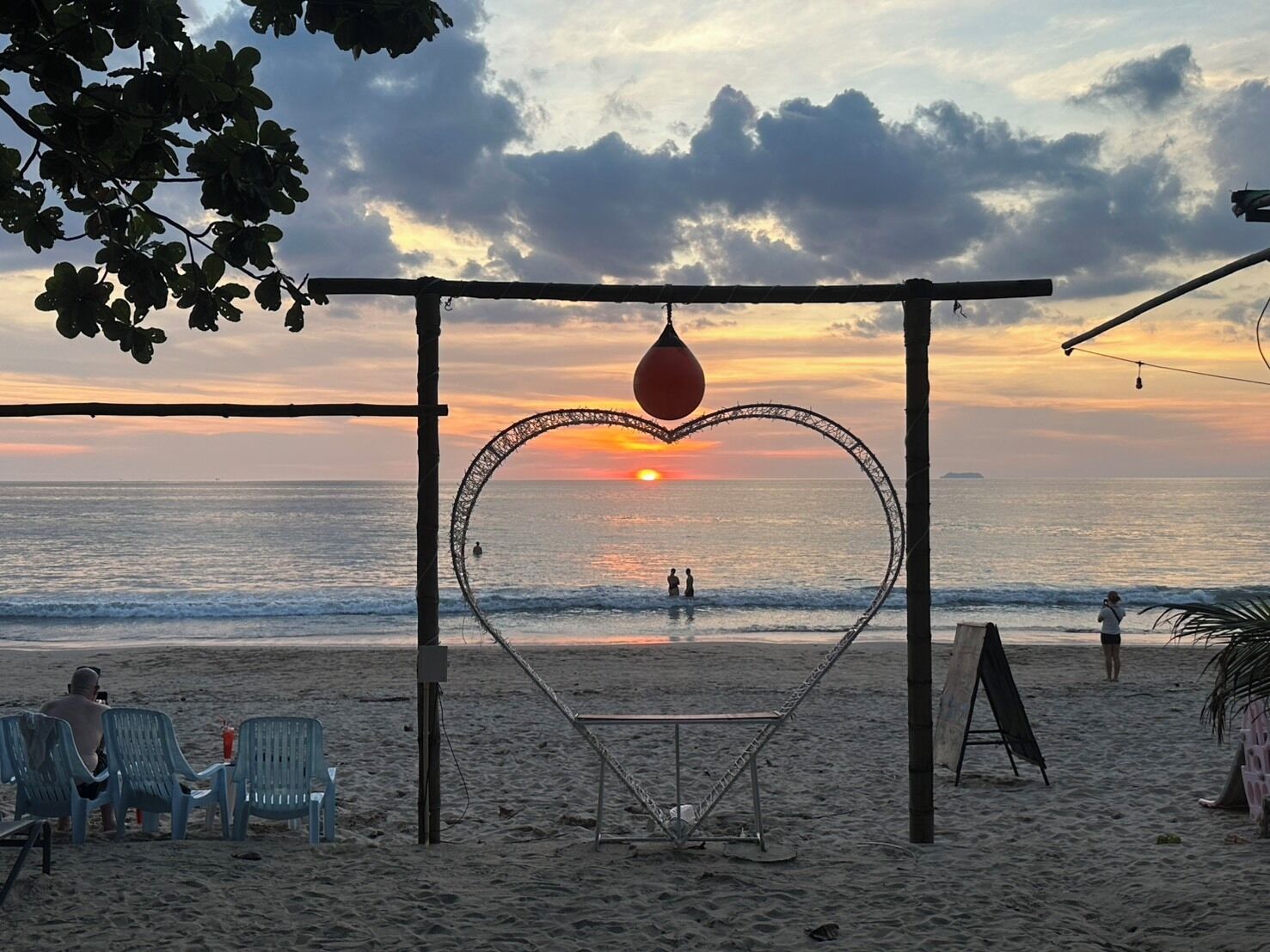 A beach with a heart-shaped structure, chairs, and a hammock.