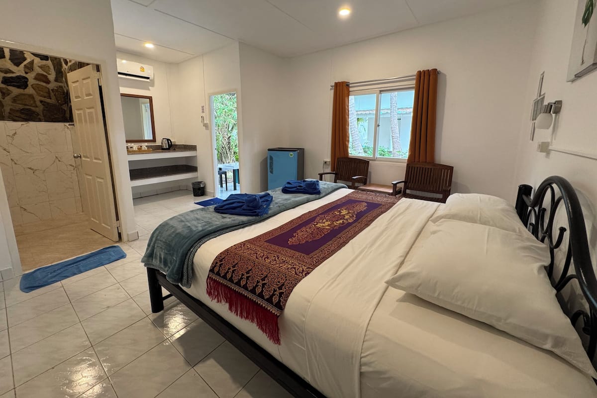 Quarto de hotel com cama, escrivaninha, cadeira, televisão pequena e banheiro com chuveiro e vaso sanitário.