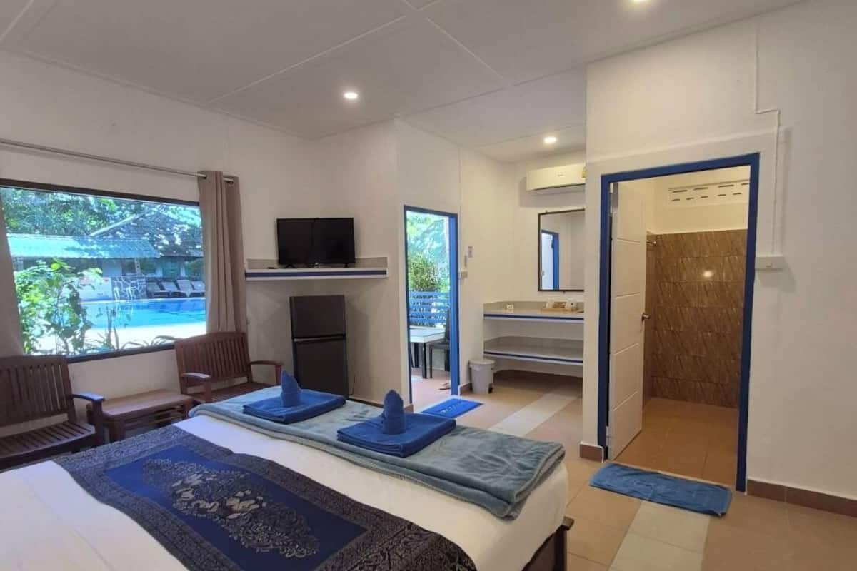 Quarto de hotel com uma cama grande, uma escrivaninha com computador, televisão e vista para o oceano.