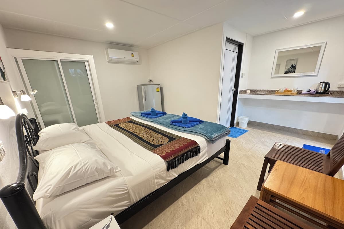 Quarto de hotel com cama, escrivaninha, cadeira, guarda-roupa e cozinha compacta.