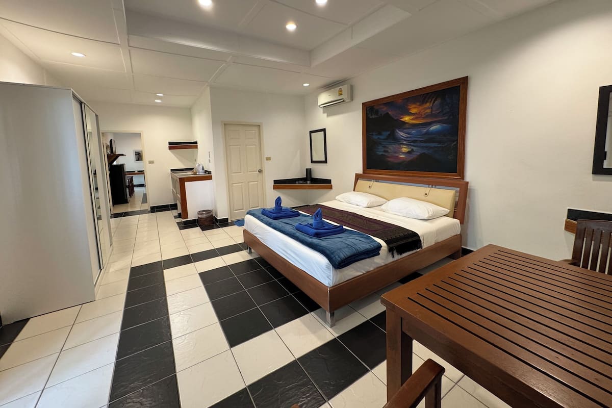 Quarto de hotel com uma cama, uma mesa de madeira, uma escrivaninha com cadeira, um quadro na parede e um ar condicionado.