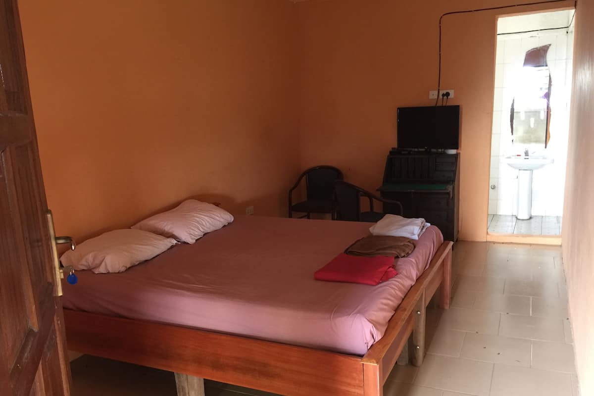 Ein Zimmer mit einem Holzbett, einem Schreibtisch mit Stuhl und einer kleinen Küchenzeile.