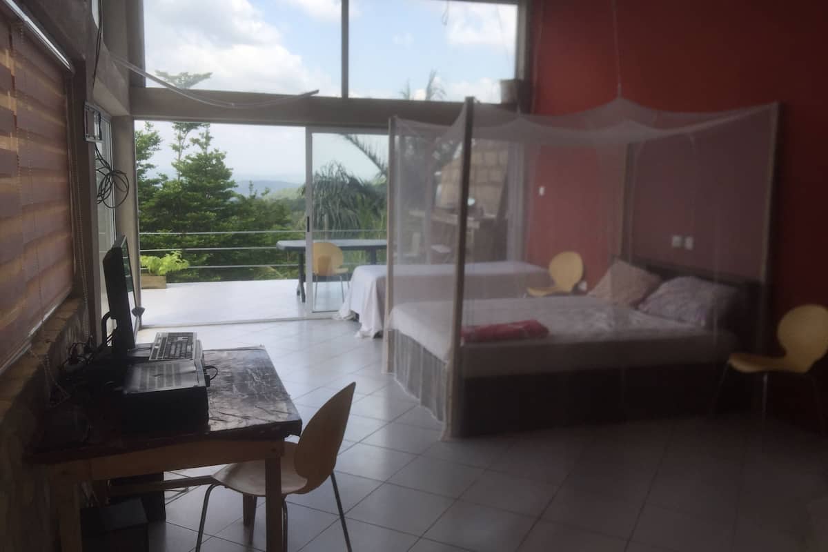 Ein Schlafzimmer mit Bett, Schreibtisch und Stuhl. Ein Balkon mit Tisch und Stühlen ist vorhanden.