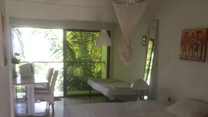 A bedroom with a bed, a bedside table, a chair, and a view of a balcony with plants. - Sweet Mother Eco Resort (Aburi)