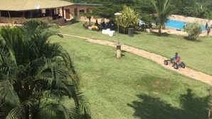 A grassy area with a pool, a building, and a person riding a quad bike. - Sweet Mother Eco Resort (Aburi)