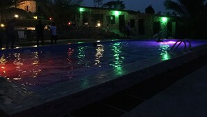 A nighttime pool area with illuminated water and surrounding buildings. - Sweet Mother Eco Resort (Aburi)