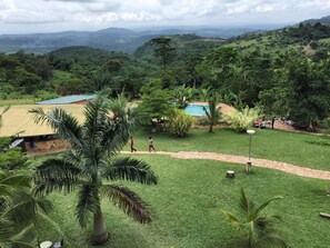 A lush green landscape with a swimming pool, palm trees, and a stone pathway. - Sweet Mother Eco Resort (Aburi)