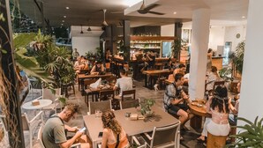 Un comedor moderno con varias mesas y sillas, rodeado de grandes macetas con plantas.