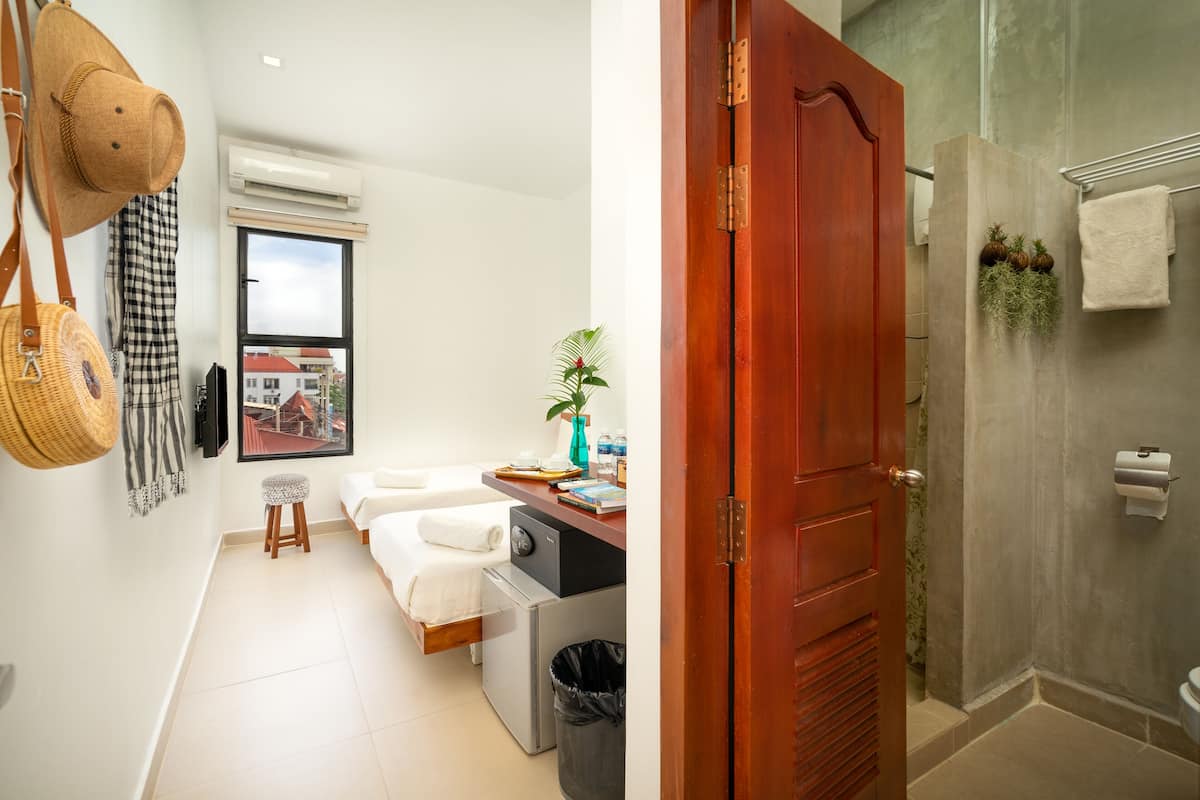 Una habitación de hotel pequeña con una cama, un taburete, una lavadora y un cubo de basura.