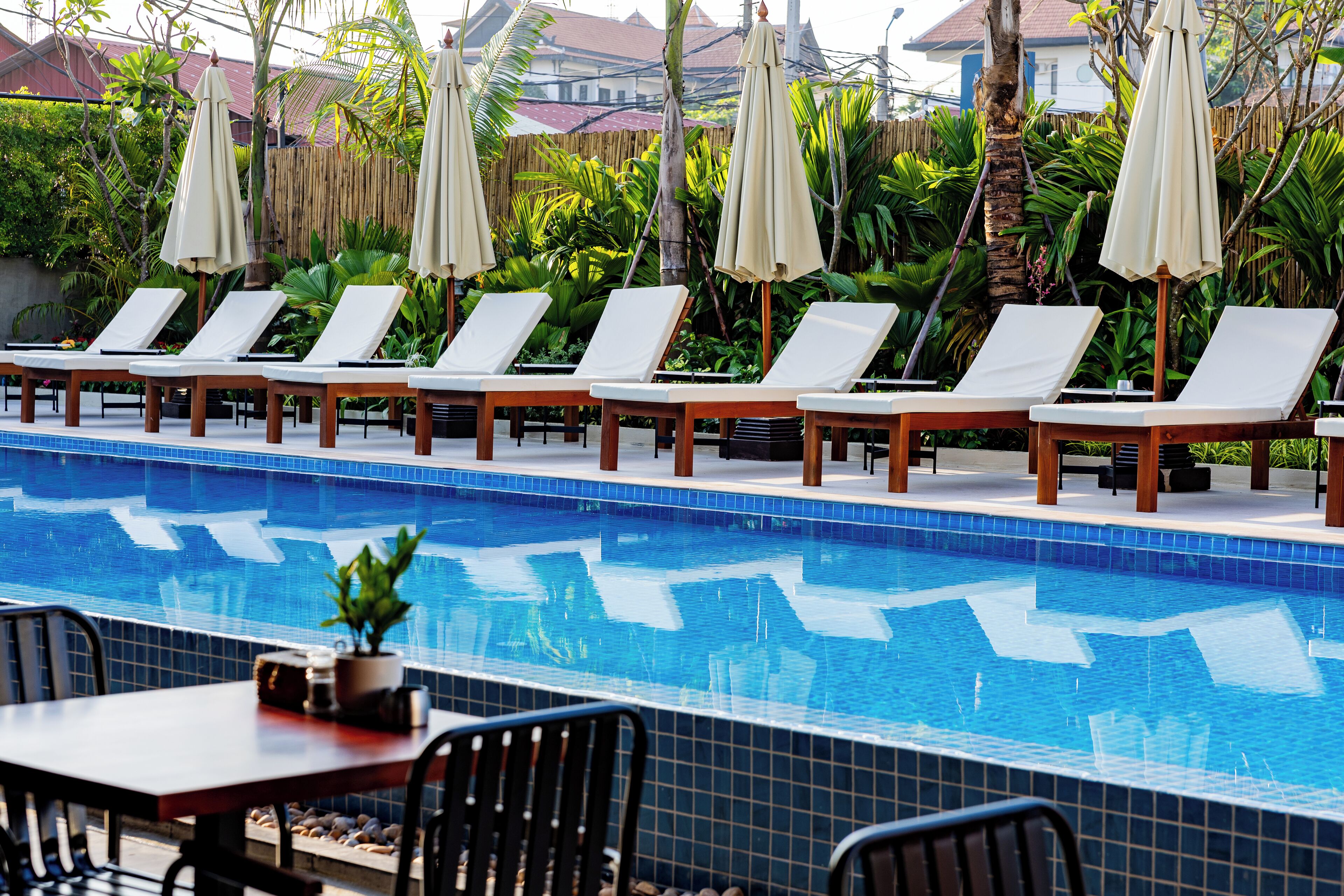 A poolside area with lounge chairs and umbrellas, a dining table, and a view of the pool.
