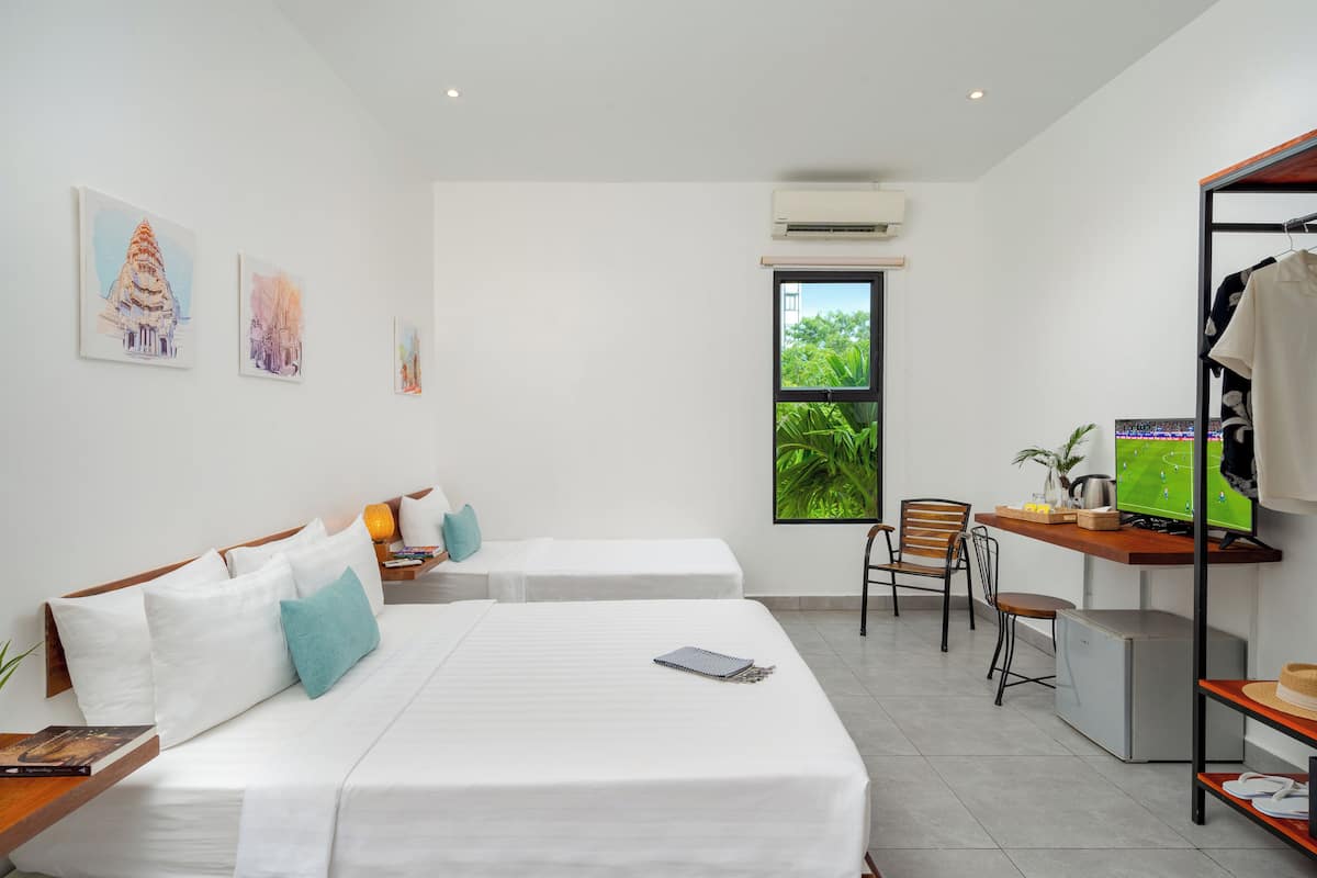 Habitación de hotel con dos camas, un escritorio con computadora, una silla y ventana con vistas a zonas verdes.