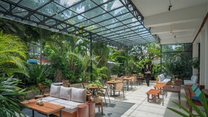 Un jardín interior con zonas de estar, mesas y techo de vidrio.