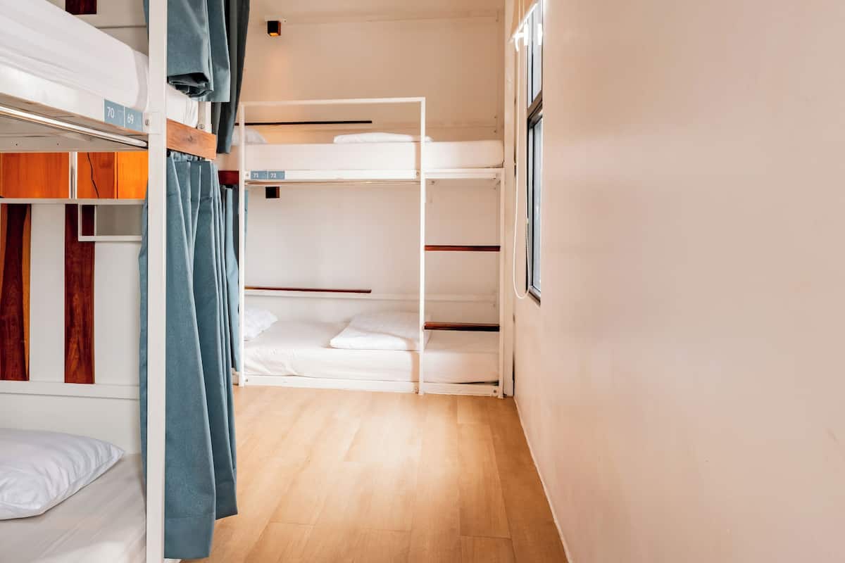 Un pasillo estrecho con literas a ambos lados, suelo de madera y una ventana a la derecha.