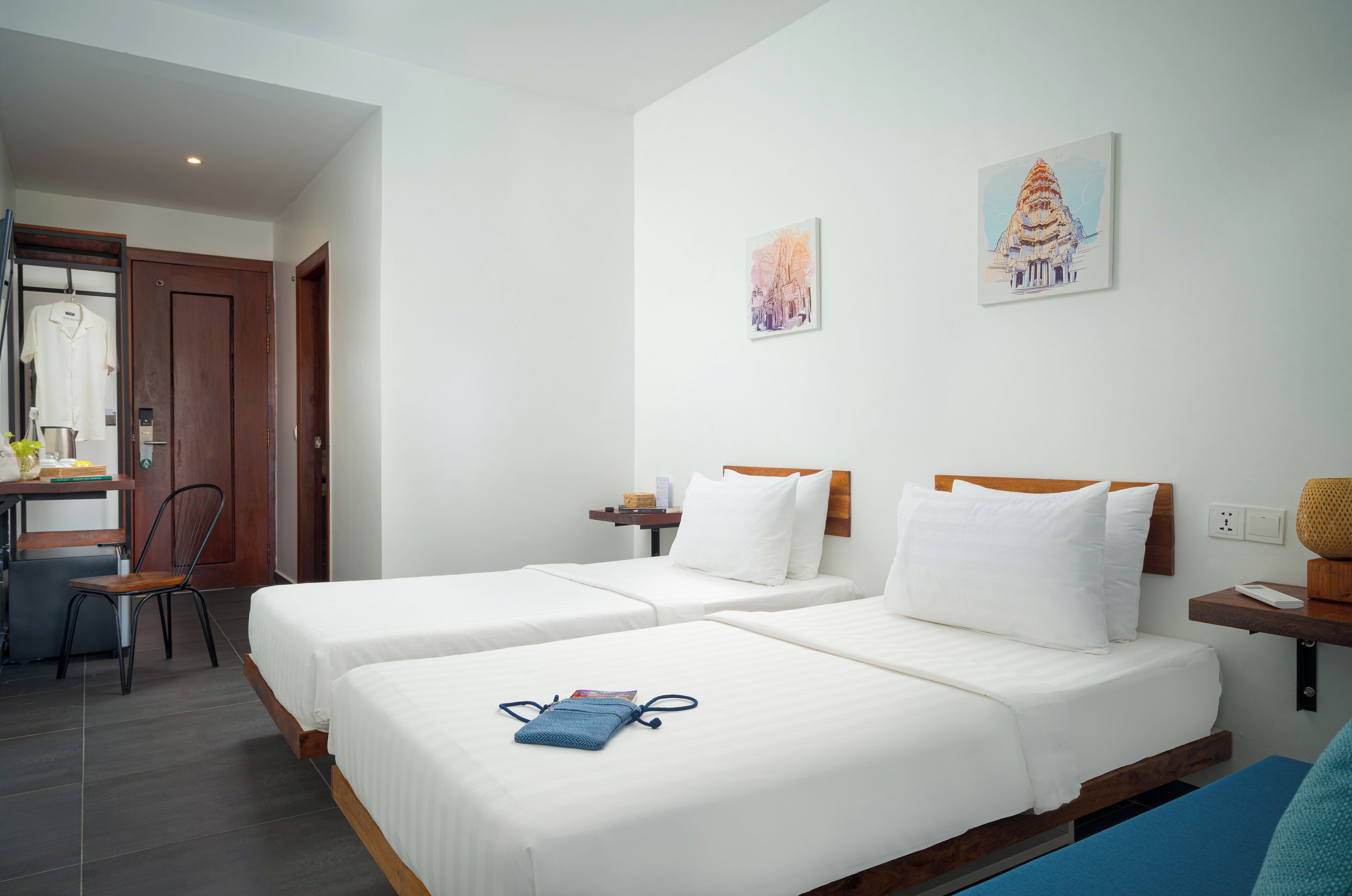 Une chambre d’hôtel avec deux lits, un bureau et une chaise. Il y a deux tableaux accrochés au mur.