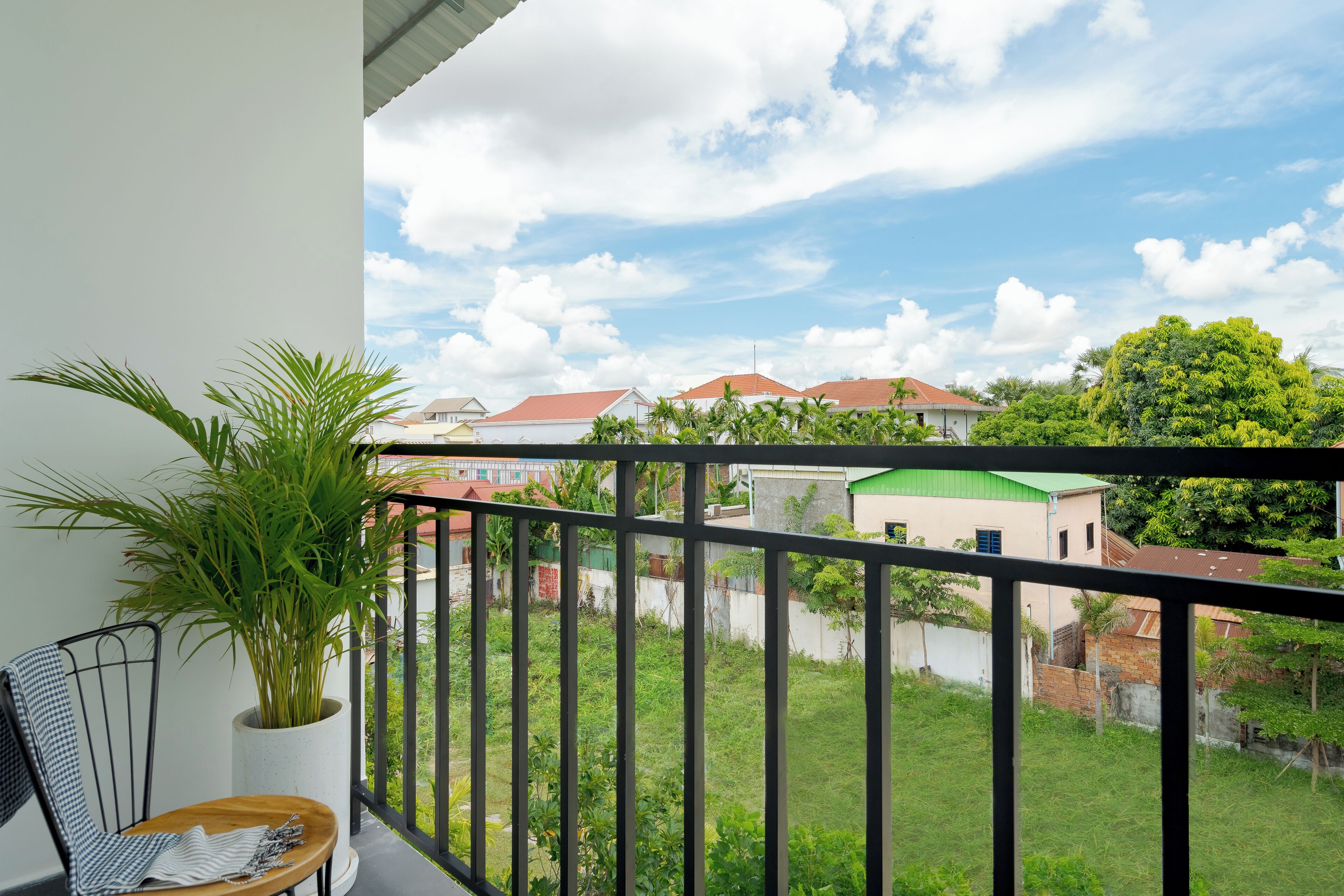 Ein Balkon mit Topfpflanze, einem Stuhl und Blick auf eine Wohngegend mit Häusern und Grünflächen.