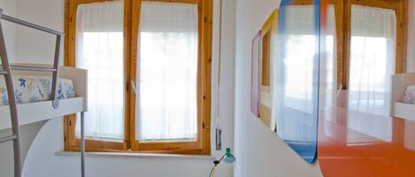 A room with bunk beds, a window with curtains, a desk with a lamp, and a mirror.