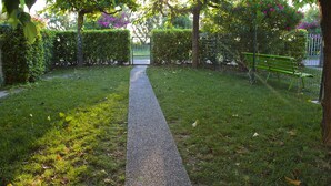 A pathway leading through a well-maintained garden area with a metal gate and a bench. - Residence Casabianca (Fermo)