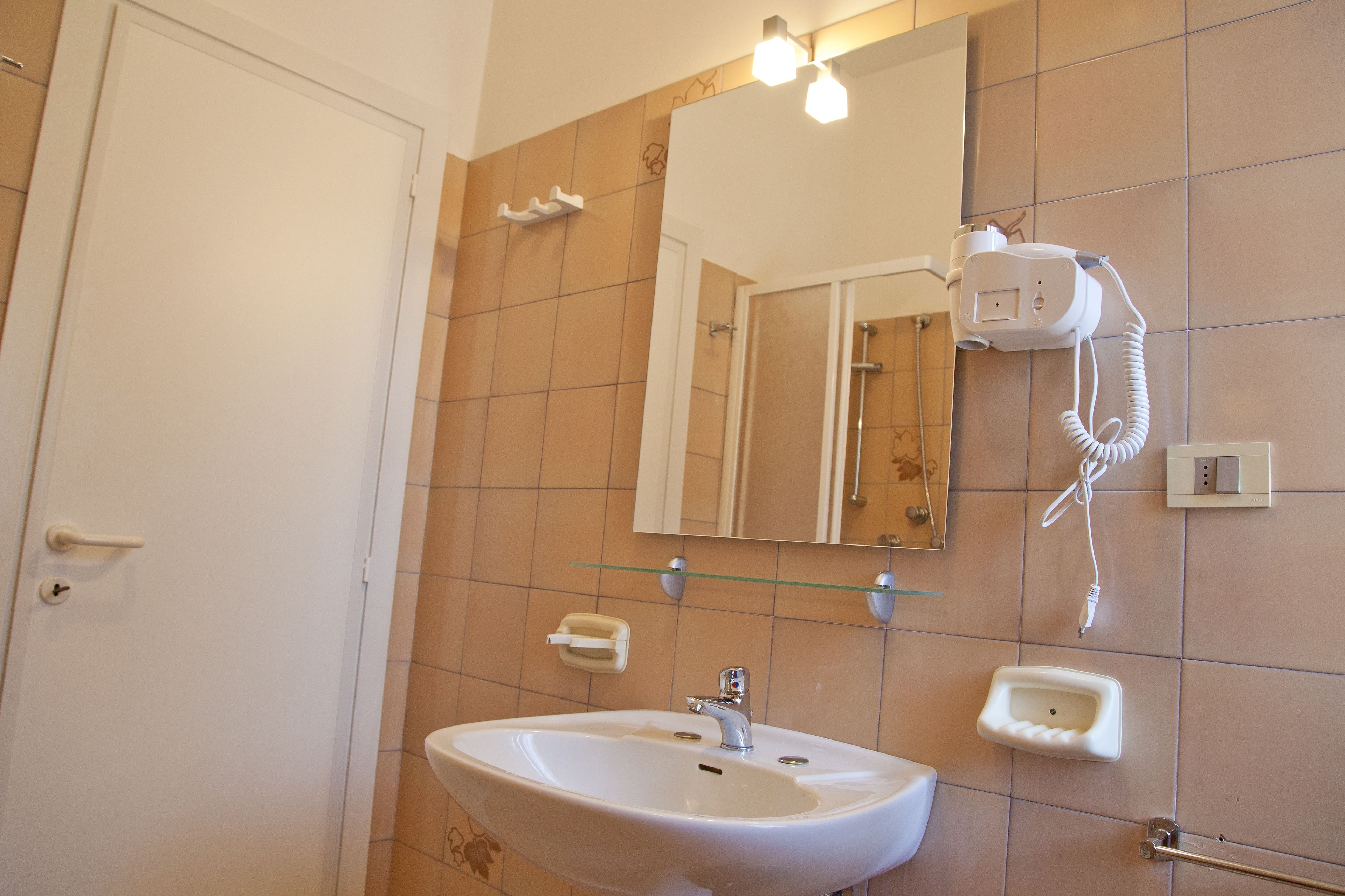 Uma casa de banho com uma pia branca, um espelho, um secador de cabelo e uma estante de vidro.