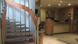 A staircase with a wooden handrail leading to a reception area with a wooden reception desk and a sign that reads "RECEPCIA". - Hotel Club (Kezmarok)