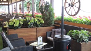 An outdoor seating area with wicker furniture, a wood-burning stove, and potted plants. - Hotel Club (Kezmarok)