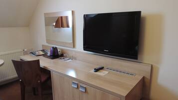 A hotel room with a wooden desk, a chair, a television, a mirror, and a radiator.