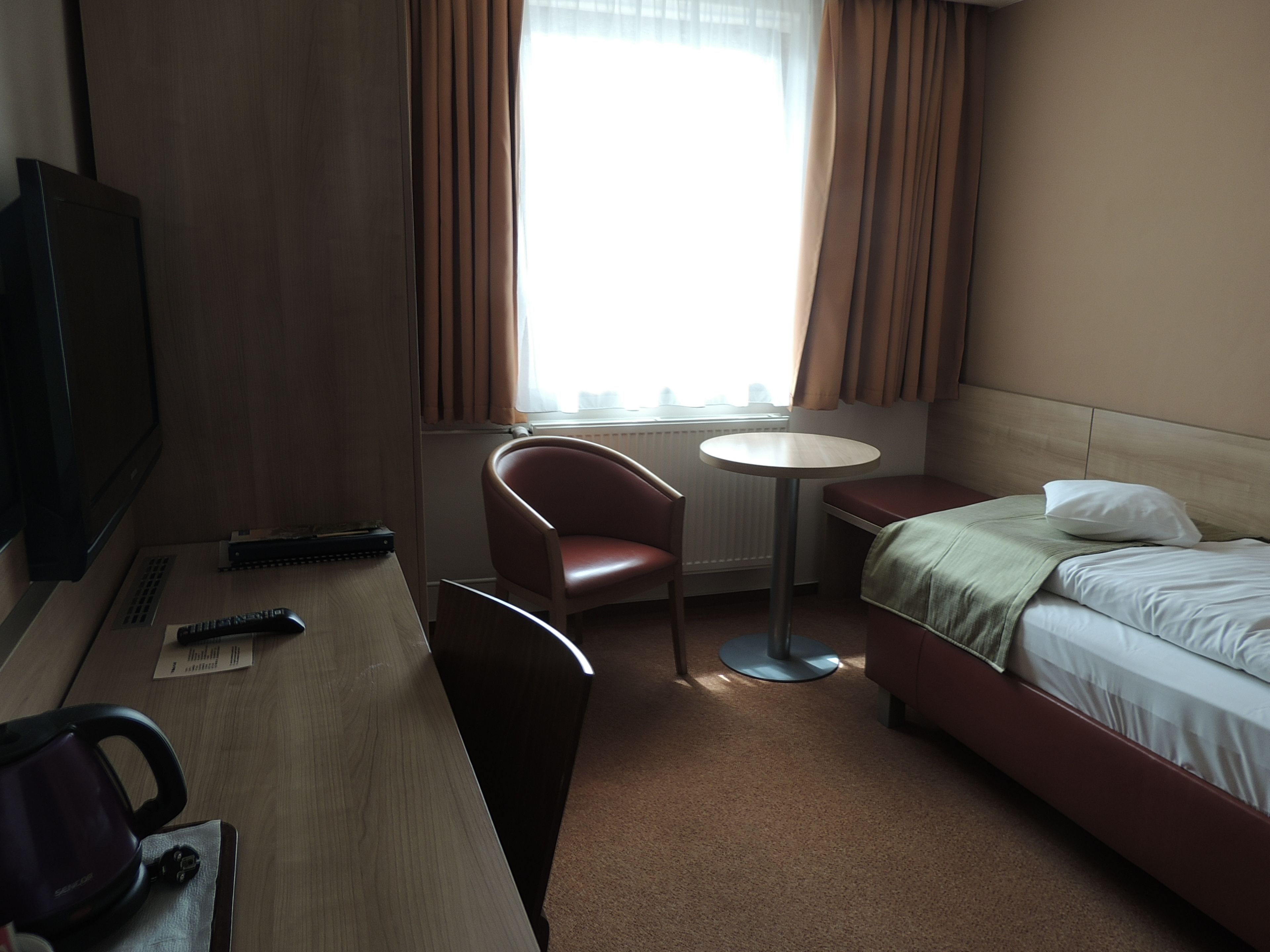 A hotel room with a bed, a desk, a chair, a TV, and a window with curtains.