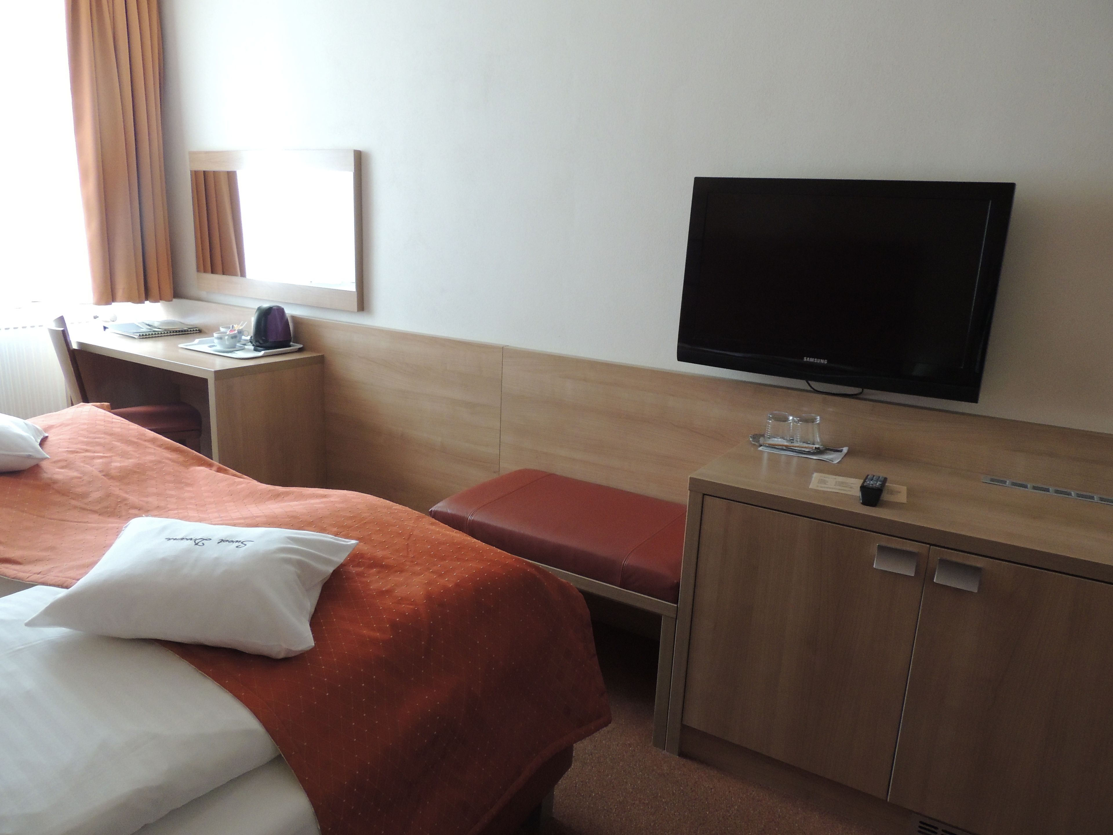 Una habitación de hotel con cama, escritorio, televisión y un armario pequeño.
