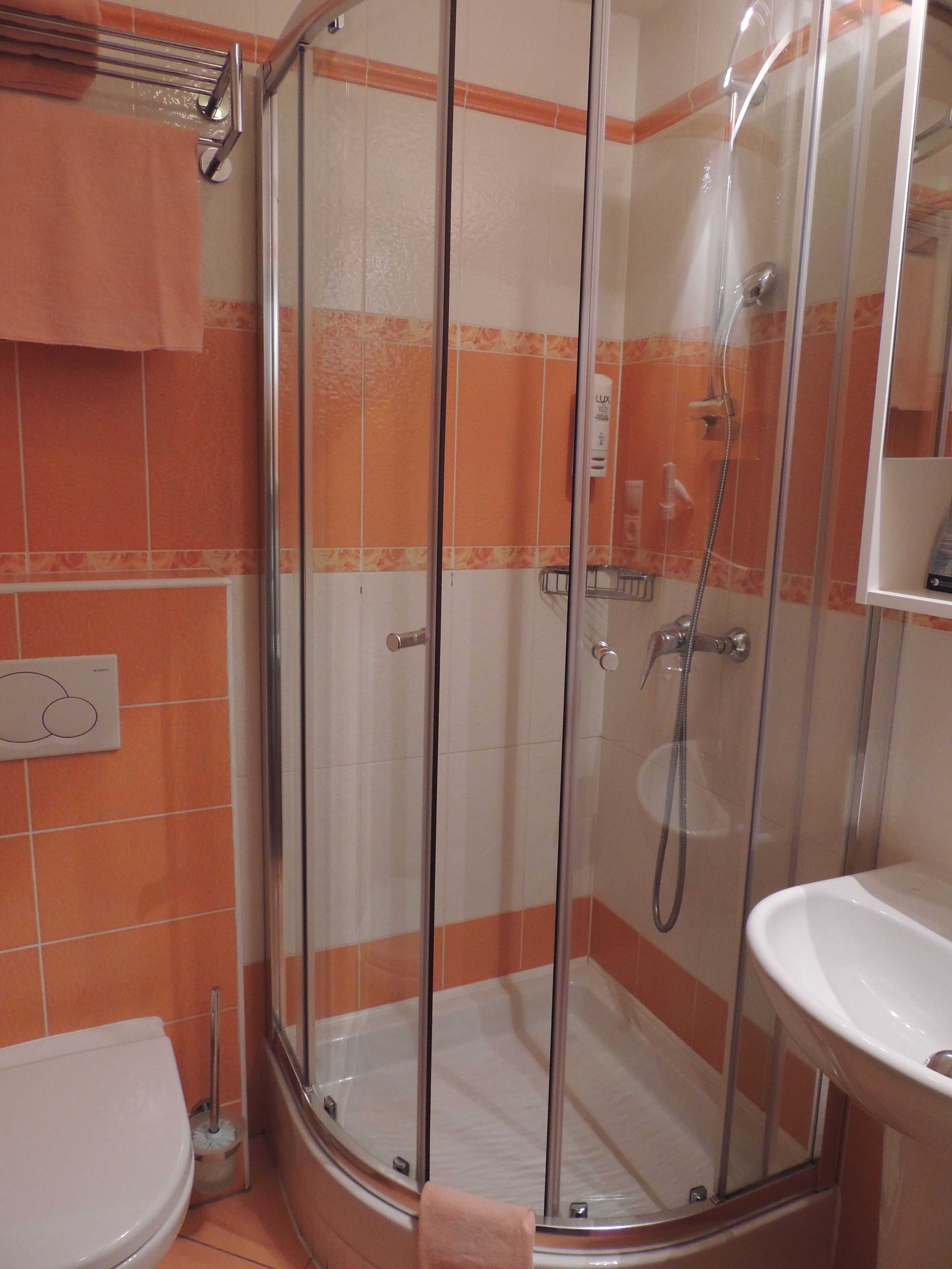 Ein Badezimmer mit einer Duschkabine, einem weißen Waschbecken und orangefarben gefliesten Wänden.