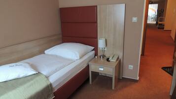 A single bed with a headboard, a bedside table with a lamp and phone, and a carpeted floor.