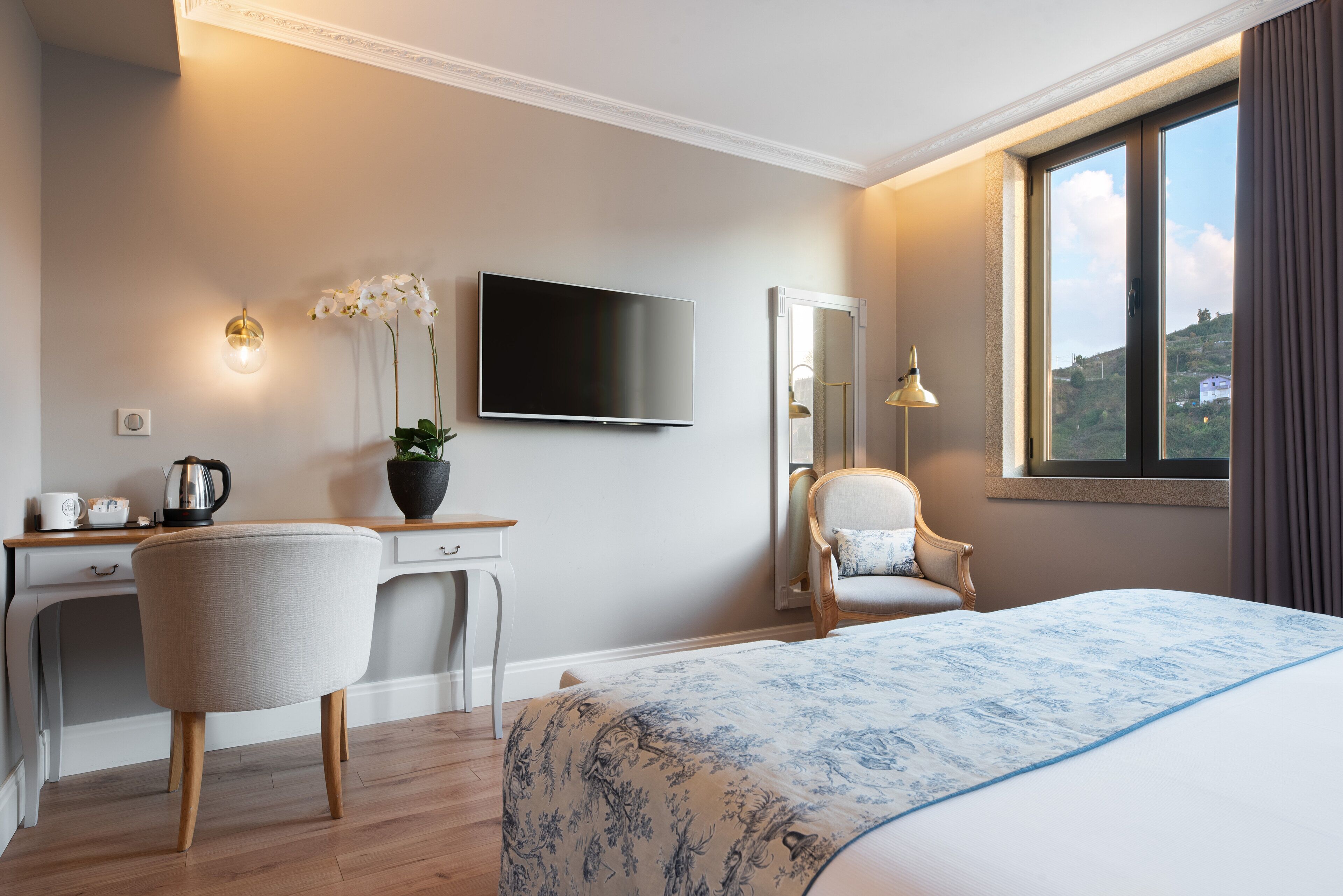 A hotel room with a bed, desk, chair, TV, and a view of the outdoors.