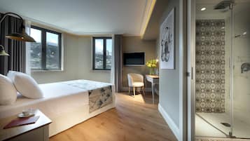 Un dormitorio moderno con cama, escritorio, silla, televisor y zona de ducha.